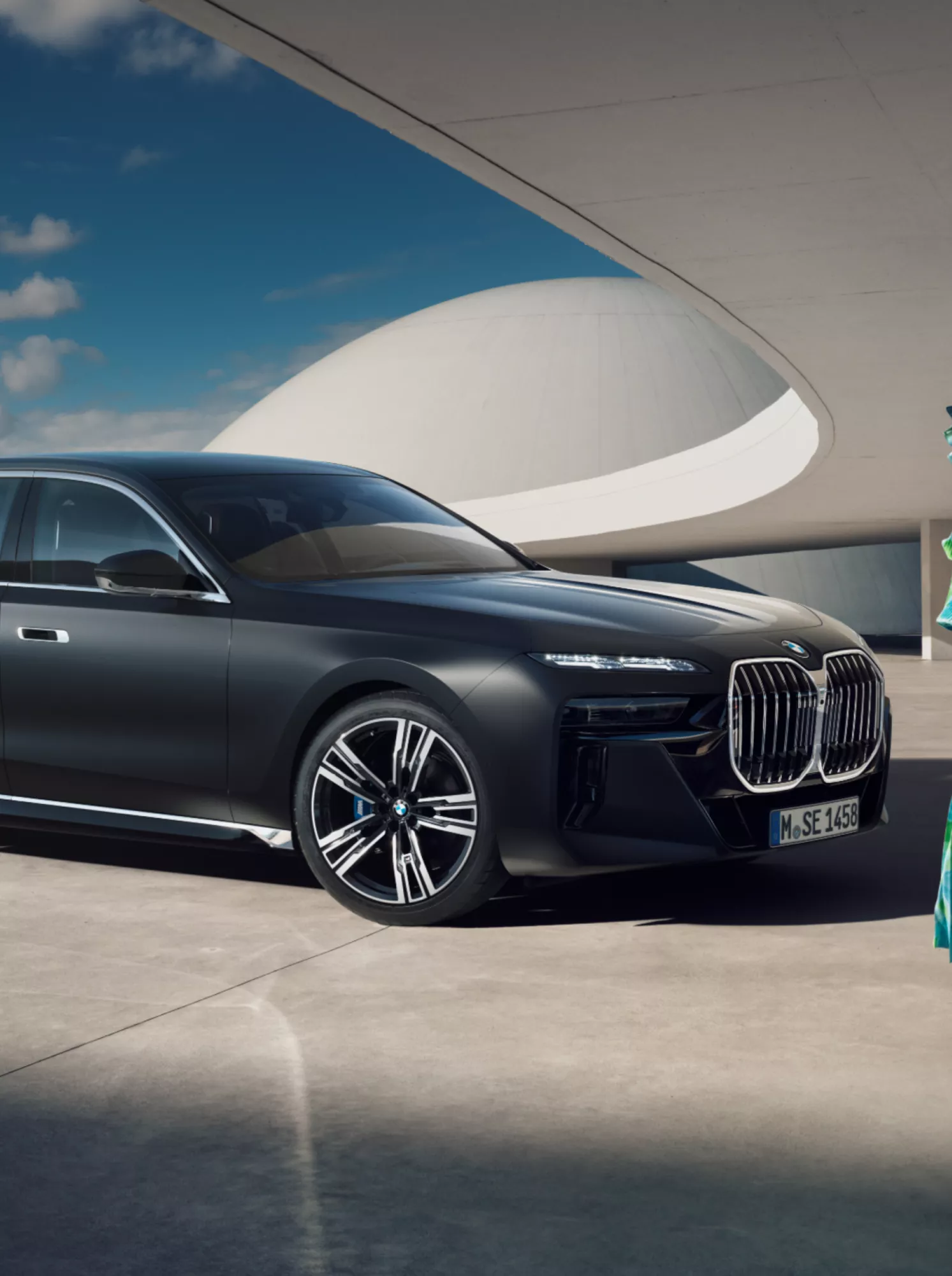 An elegantly dressed woman stands in front of a parked BMW