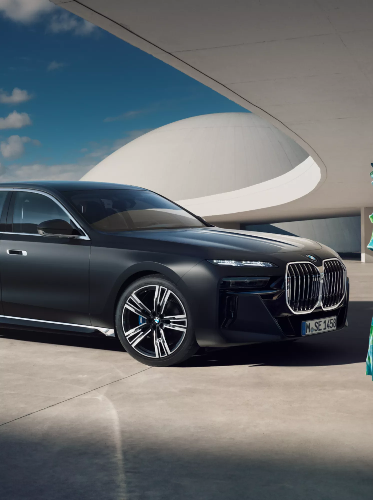 Eine Frau in einem eleganten Kleid steht vor einem parkenden BMW