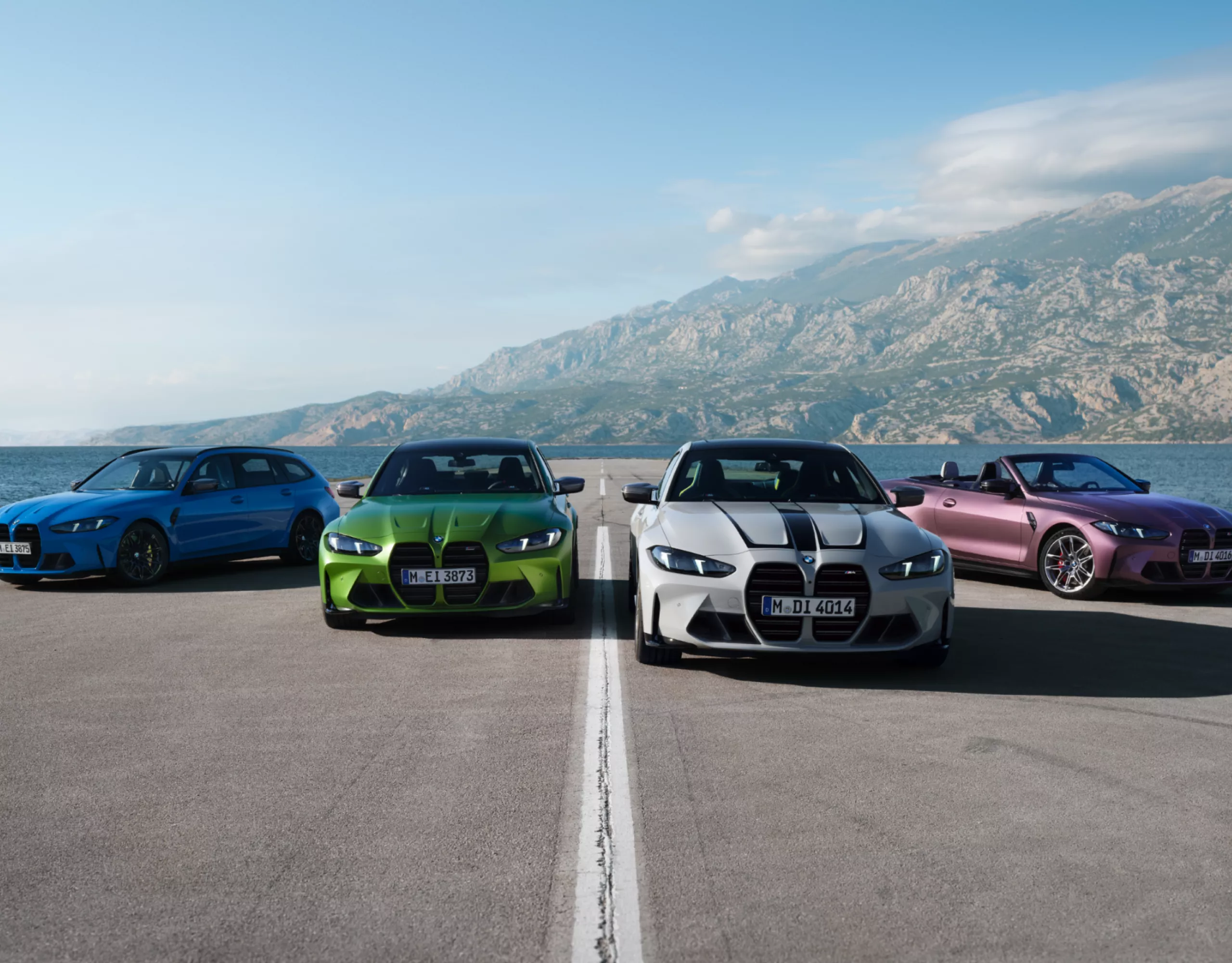 Four sporty BMWs parked against a backdrop of a lake and mountains