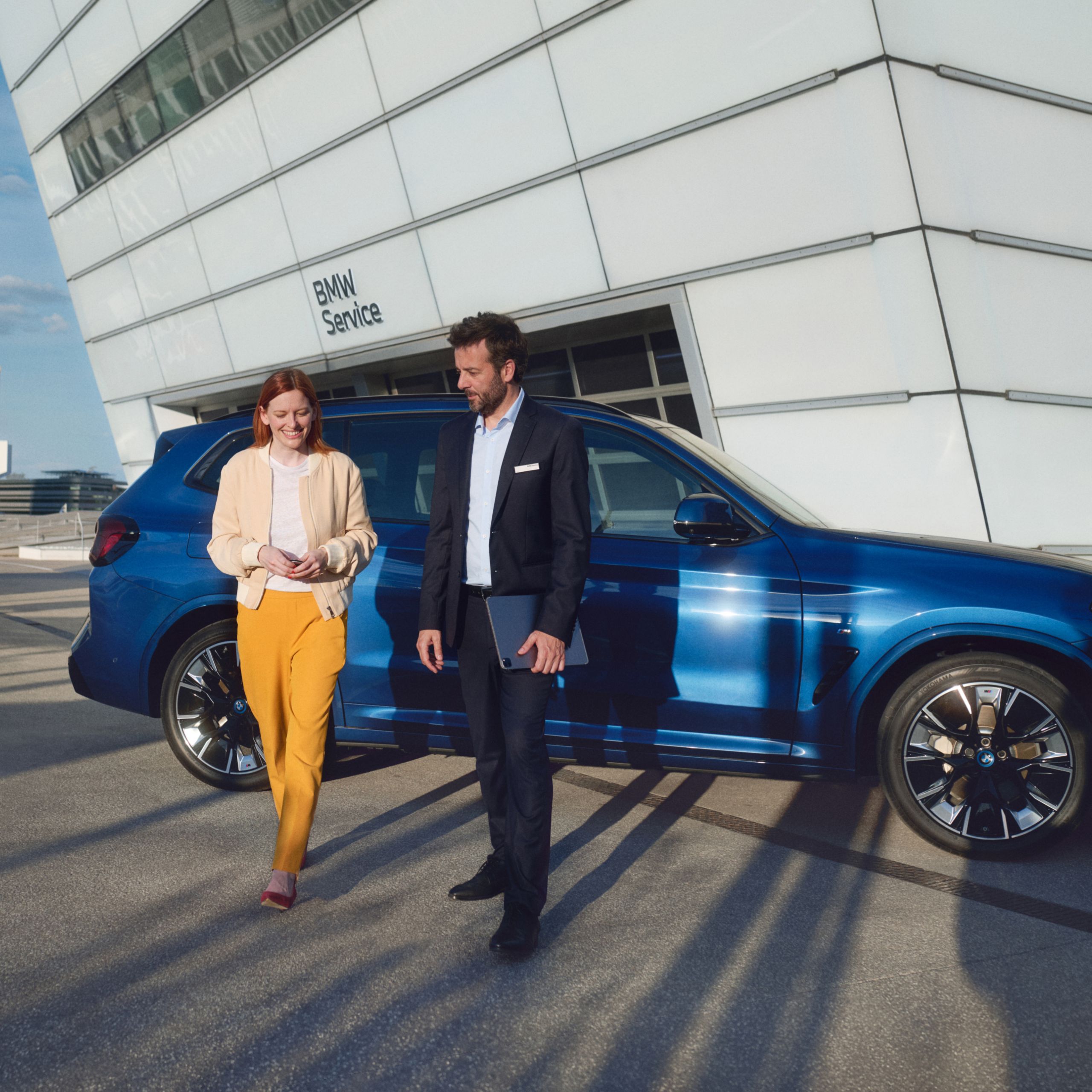 Hombre y mujer delante de un SUV de BMW frente a un taller autorizado de BMW
