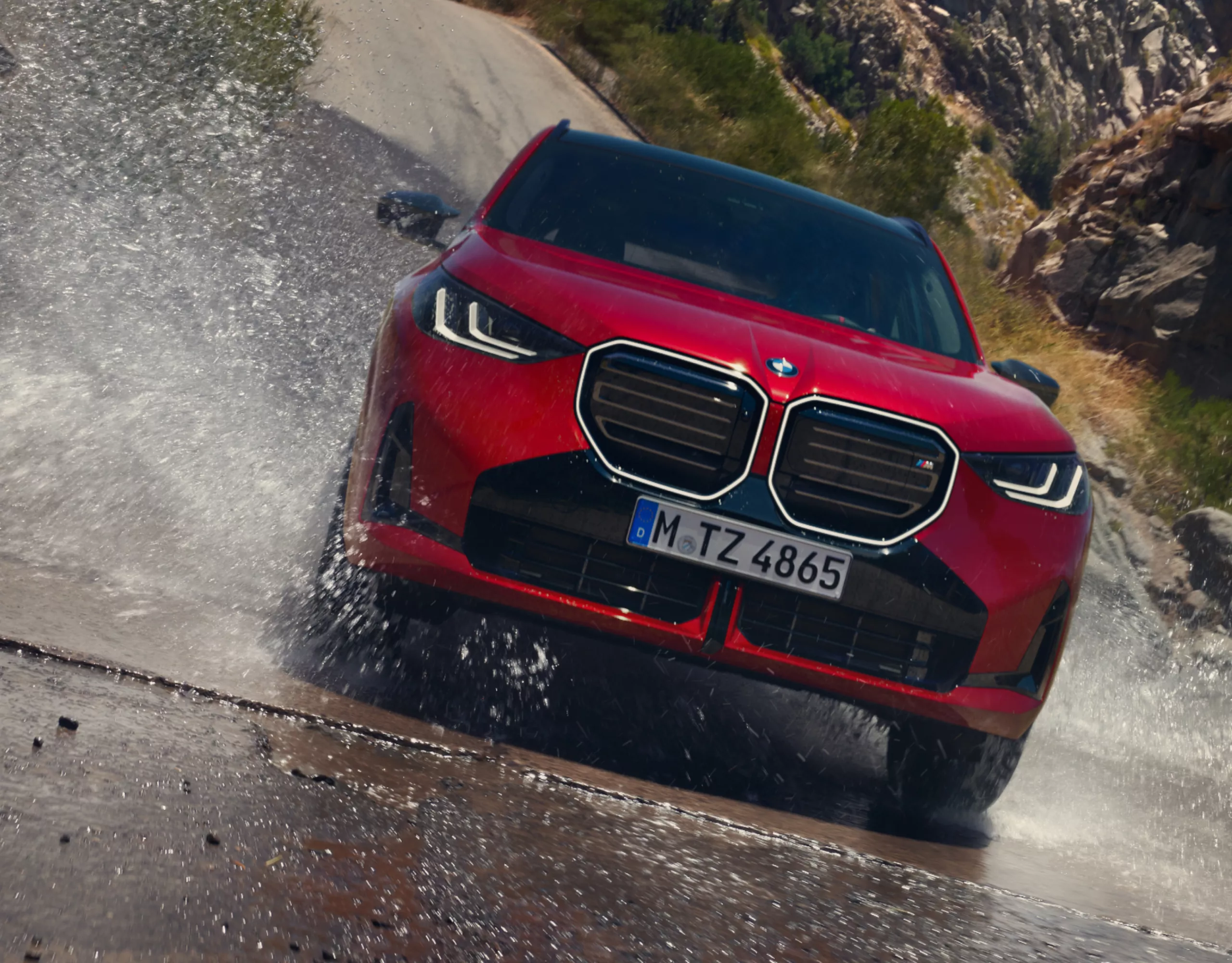 A BMW SUV splashes through a puddle on a mountain road