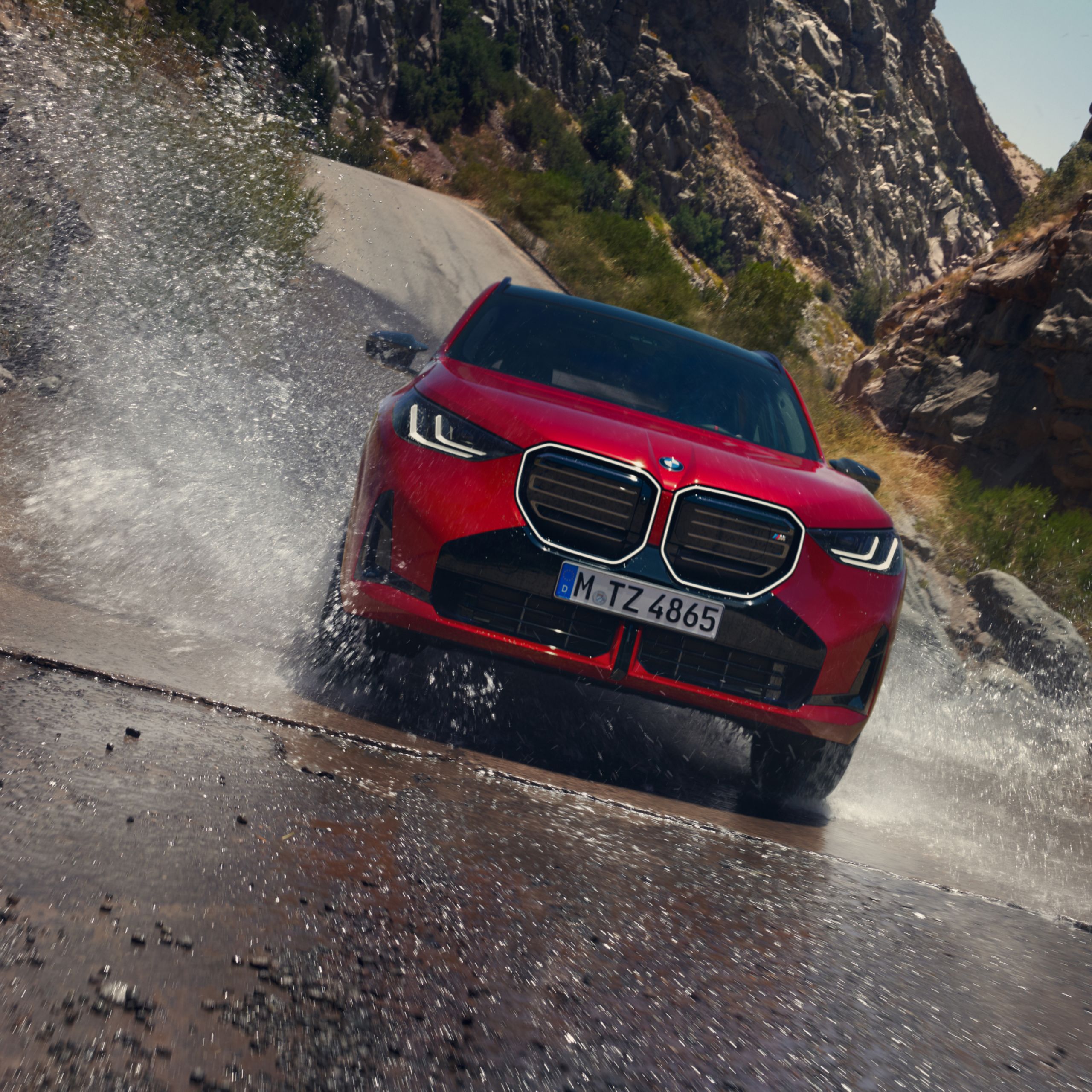 Un SUV de BMW salpicando al pasar por un charco en una carretera de montaña