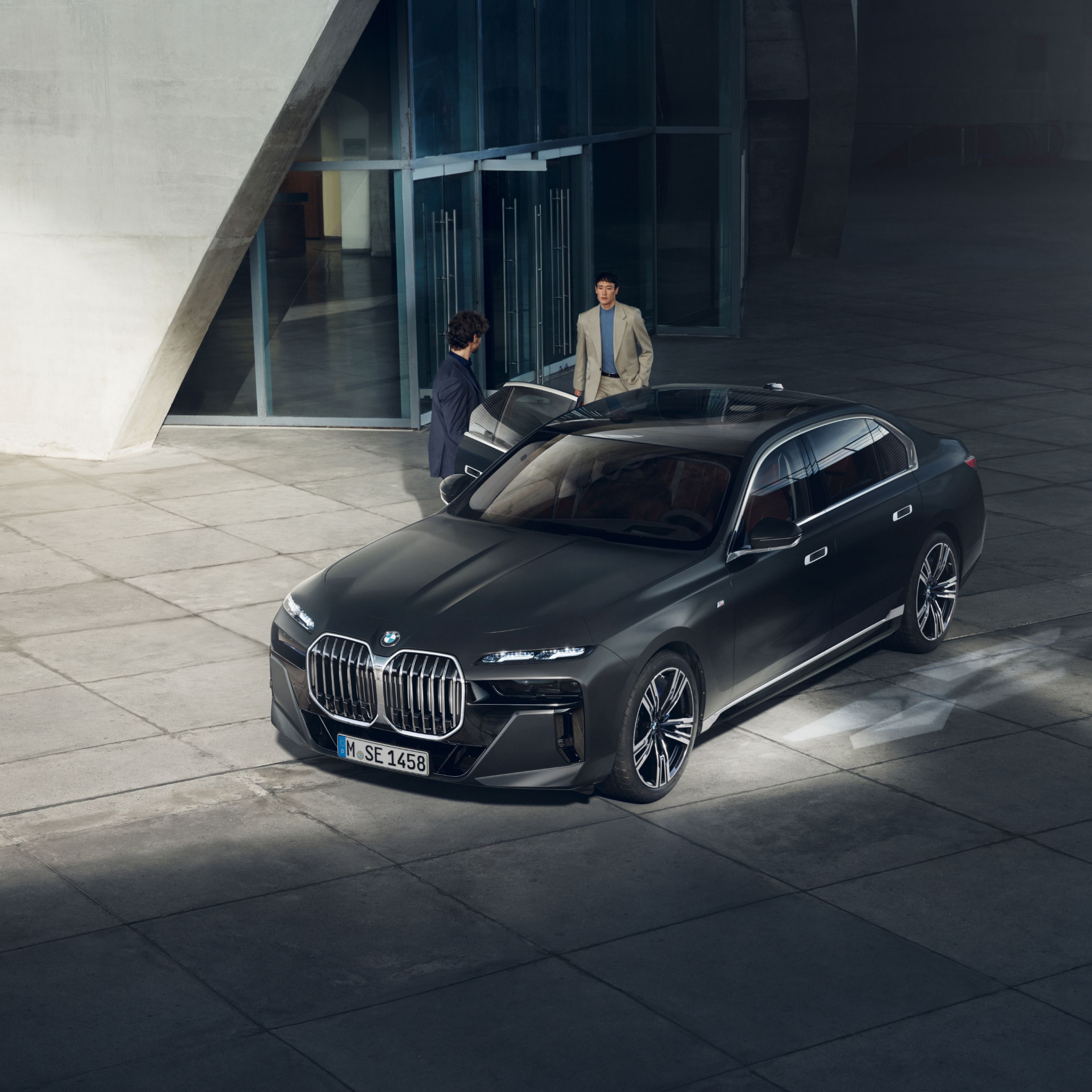Widok z góry dwóch osób obok pojazdu dyplomatycznego BMW przed budynkiem