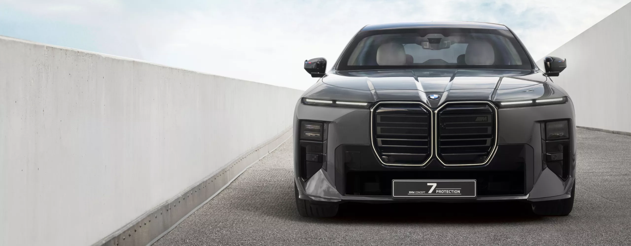 A front view of a grey BMW Concept 7 Protection parked on grey tarmac between two white walls.