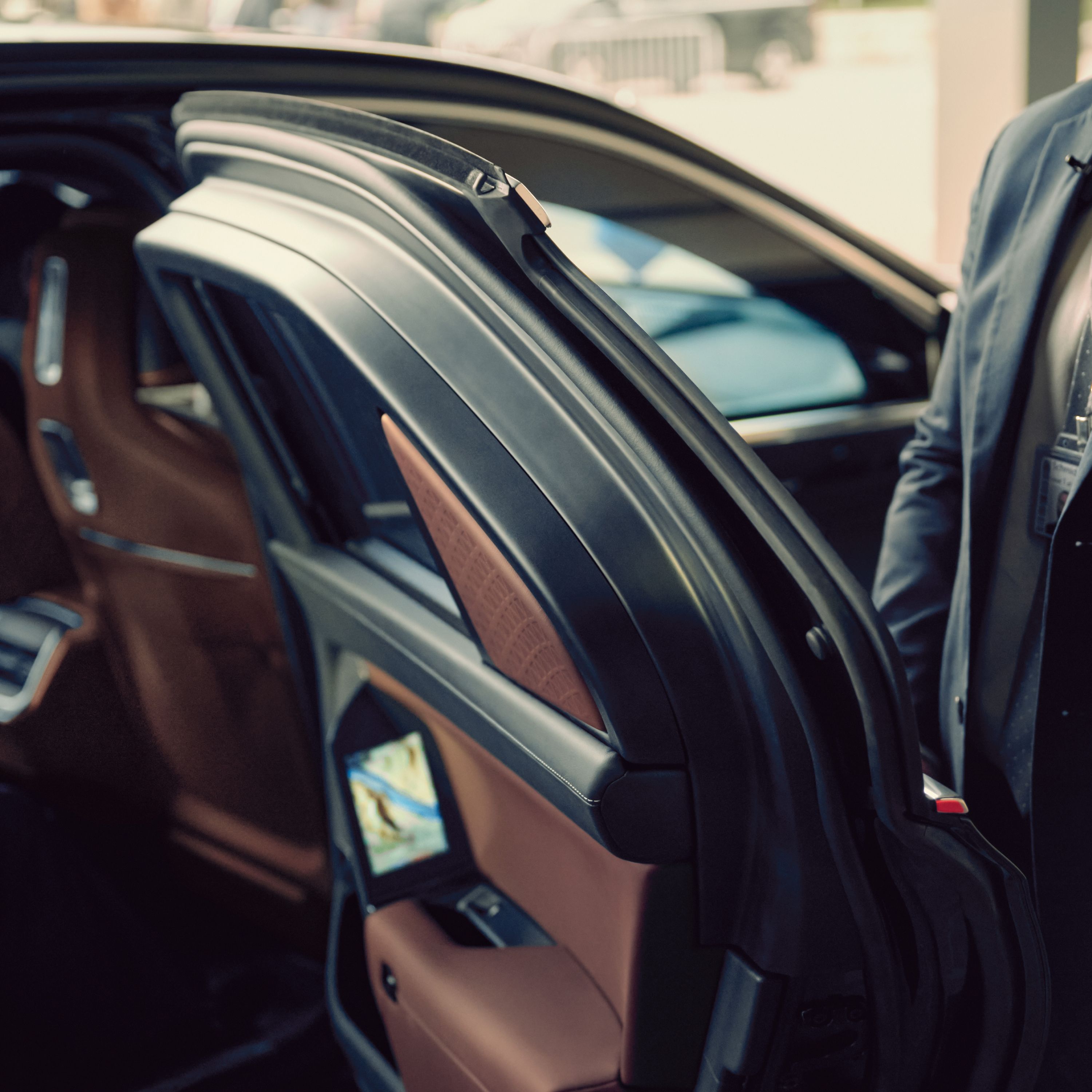 A close-up of a BMW door held open by a person in a suit