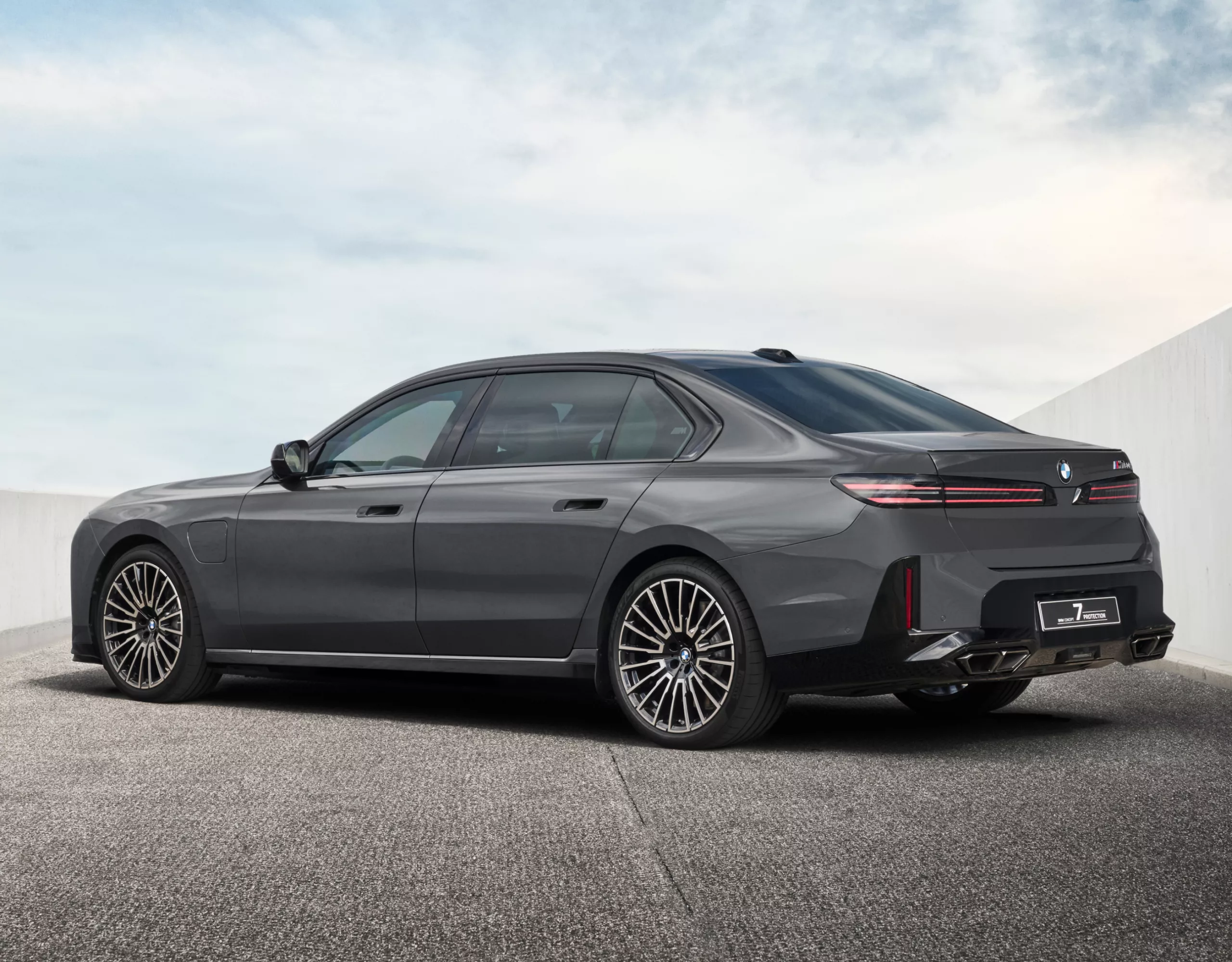 A three-quarter rear view of a grey BMW Concept 7 Protection parked on grey tarmac between two white walls.