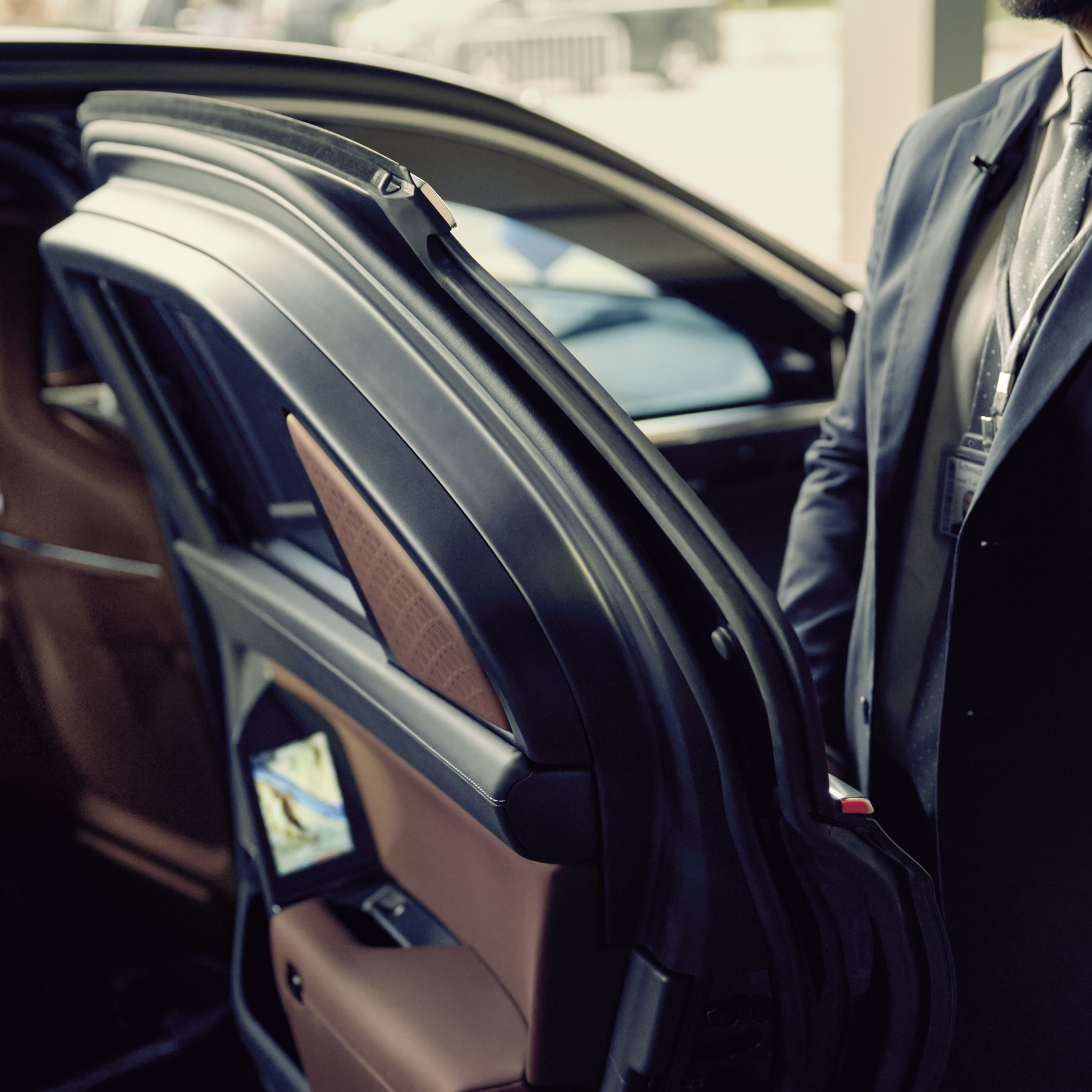 A close-up of a BMW door held open by a person in a suit