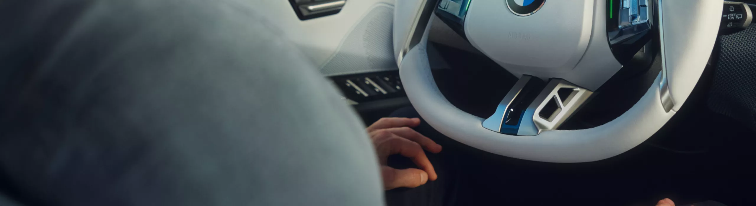 Poste de conduite d'une BMW iX3, l'aide à la conduite étant activée sur l'écran. Les mains du conducteur ne sont pas sur le volant.