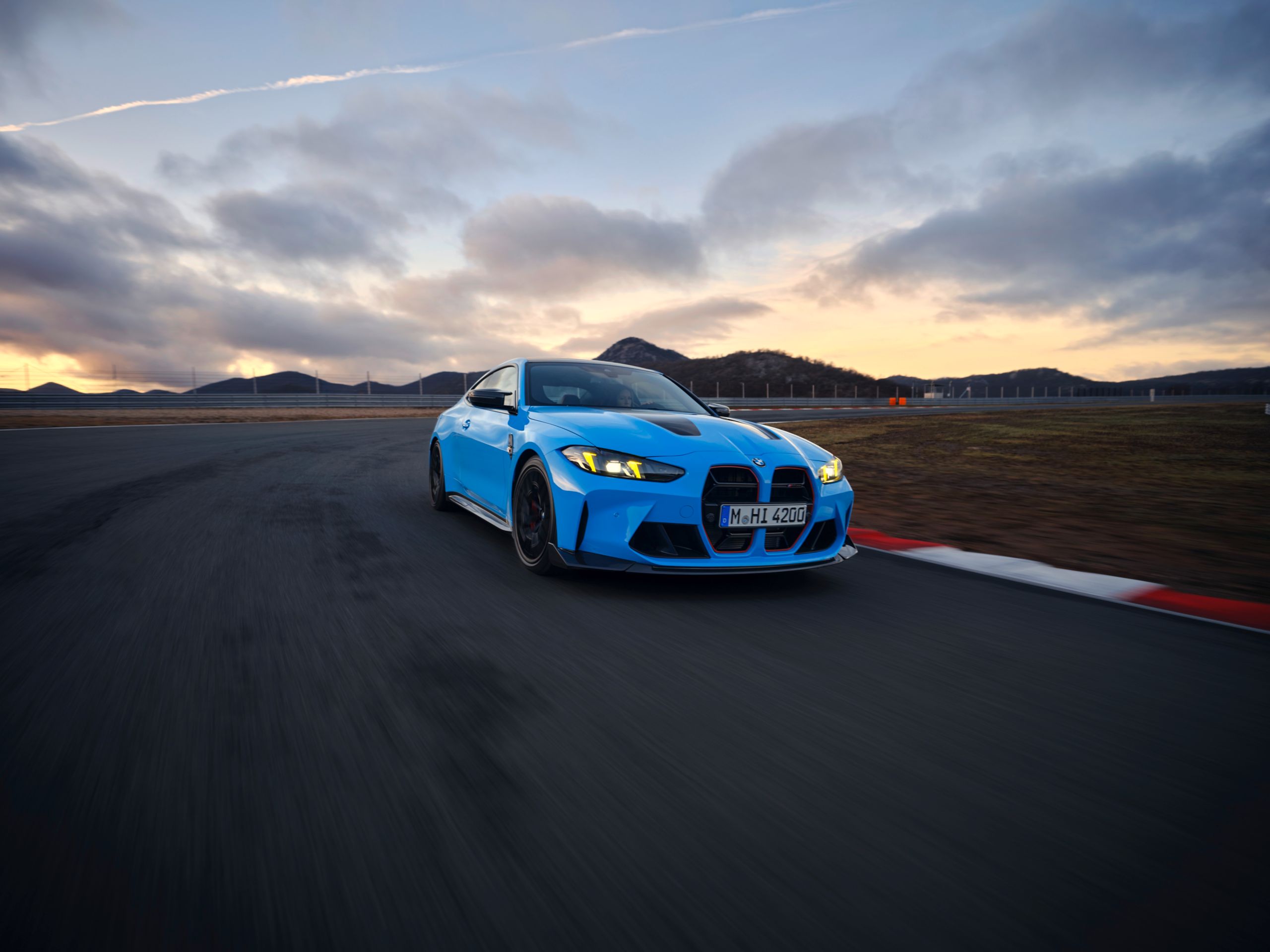 Sportowe, niebieskie BMW M4 na torze wyścigowym na tle zachodzącego słońca.