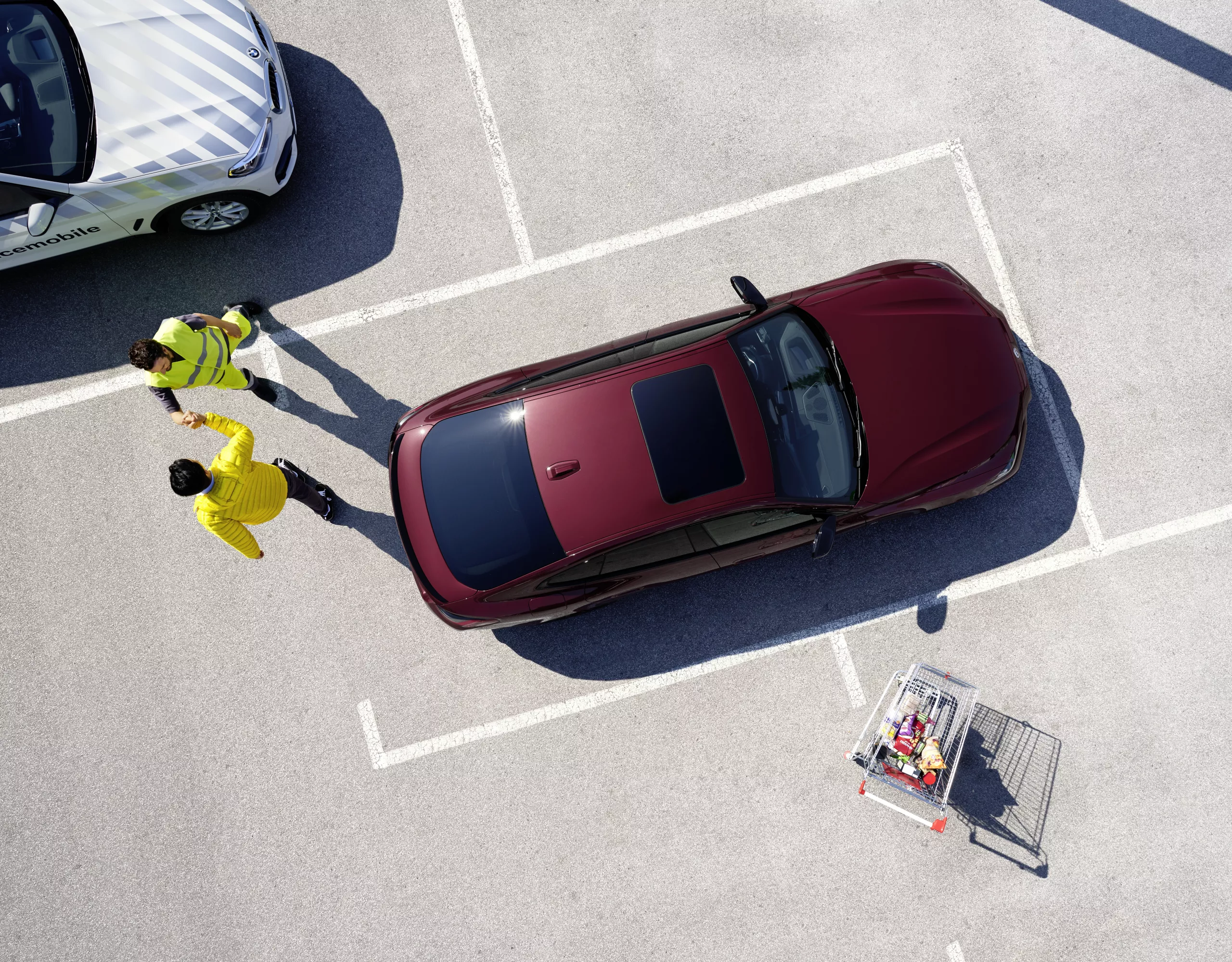 A woman sits in a BMW with the door open. A man leans on the vehicle with a house visible in the background