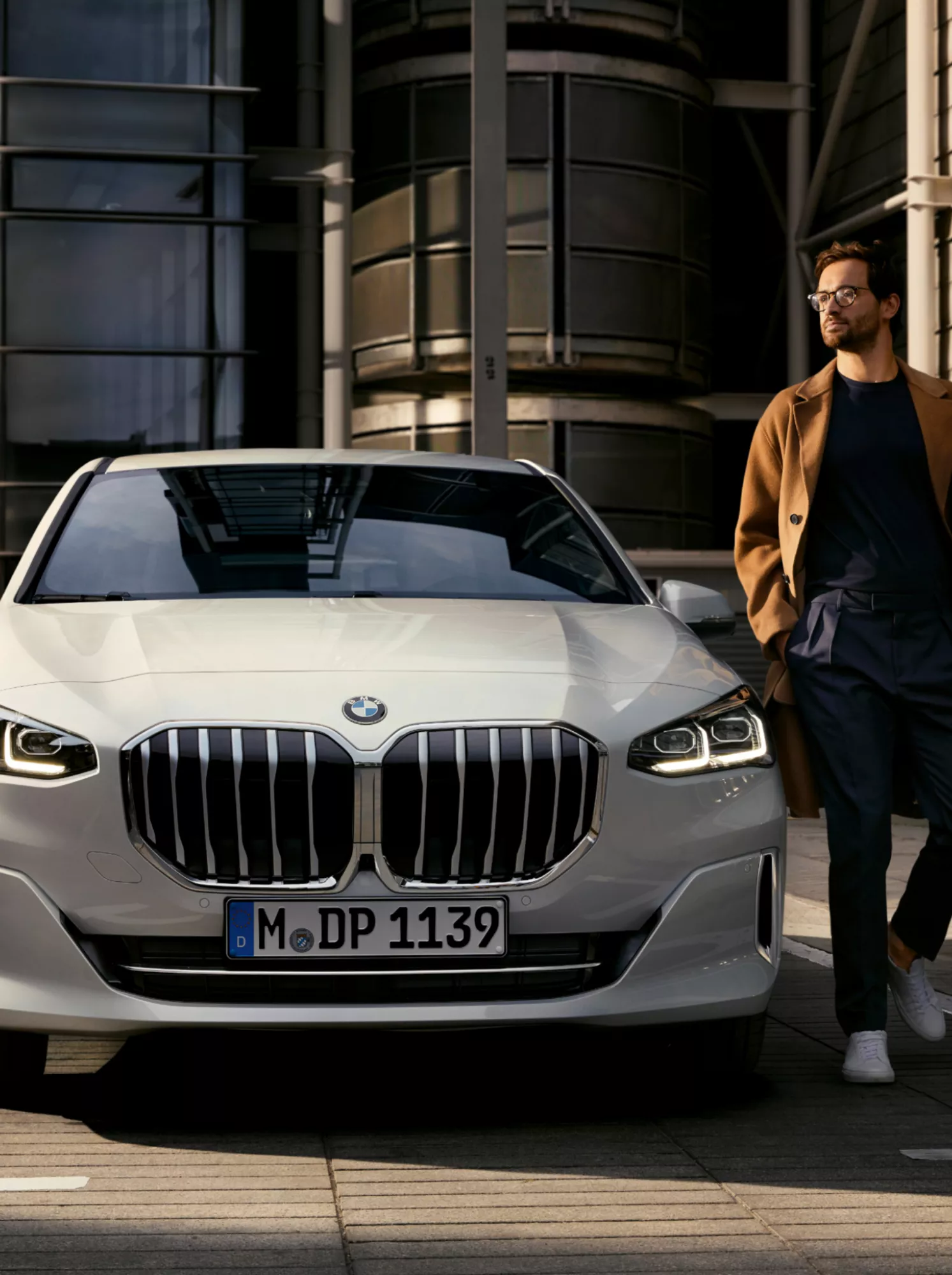 Person entfernt sich von einem BMW 2er Active Tourer welcher vor modernem Mehrfamilienhaus parkt 