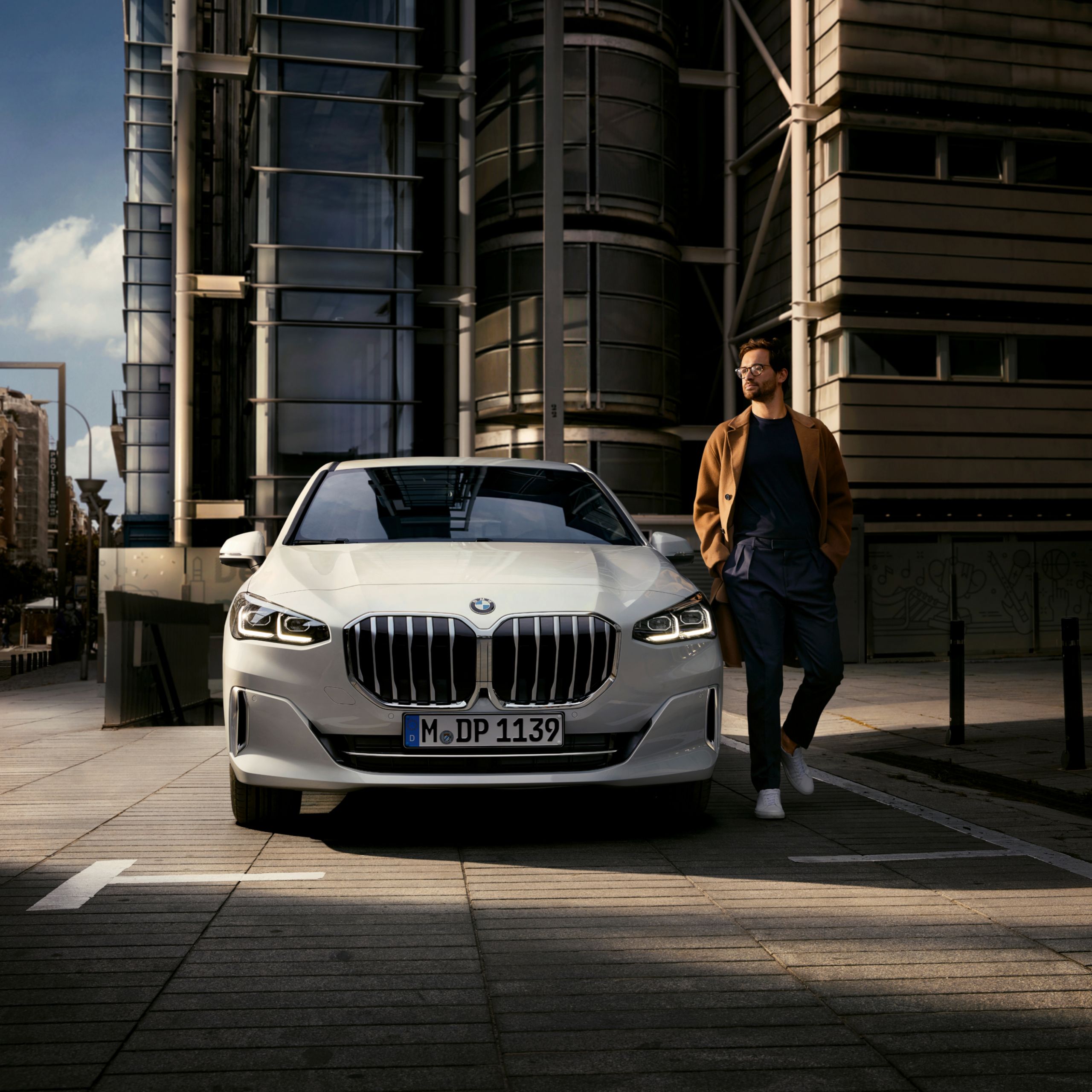 Persoon loopt weg van een BMW 2 Reeks Active Tourer die geparkeerd staat voor een modern flatgebouw 