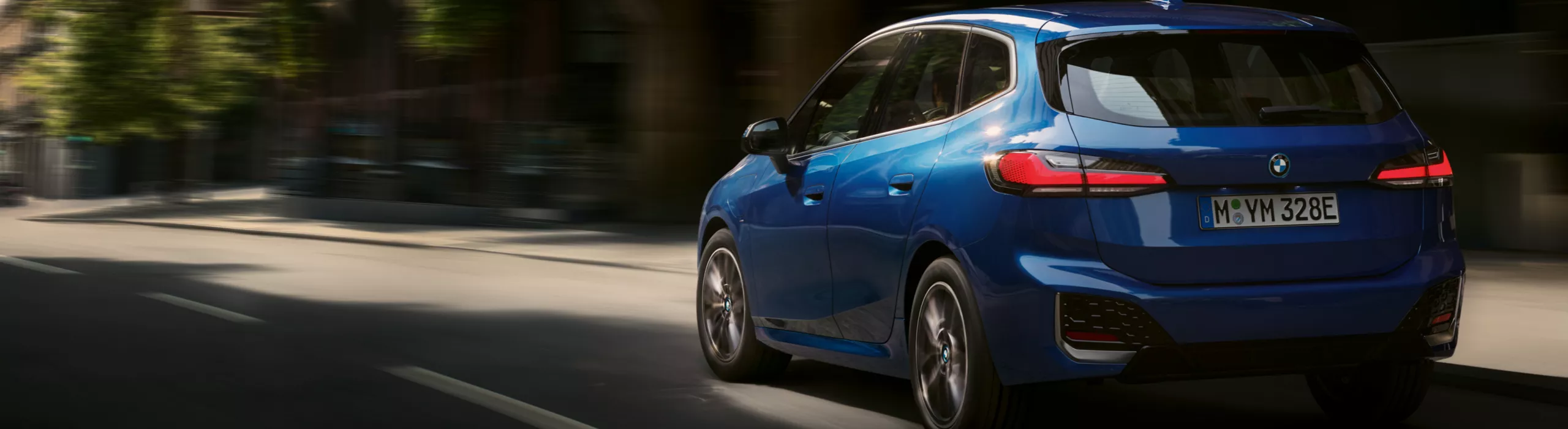 BMW 2er Active Tourer Plug-in-Hybrid fährt auf Straße vor begrüntem Parkhaus