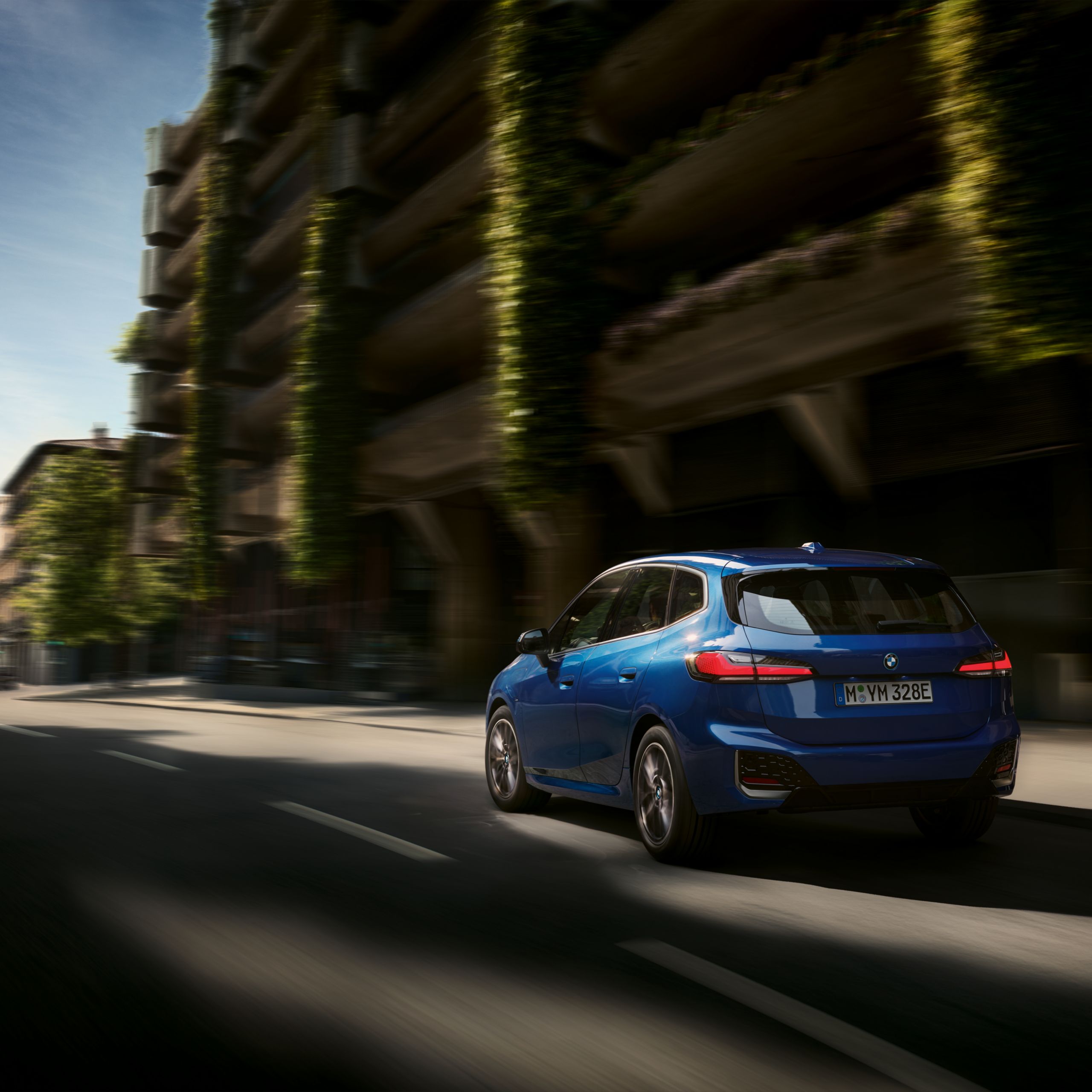 BMW 2 Reeks Active Tourer Plug-in Hybride rijdt op de weg voor een met planten begroeide parkeergarage