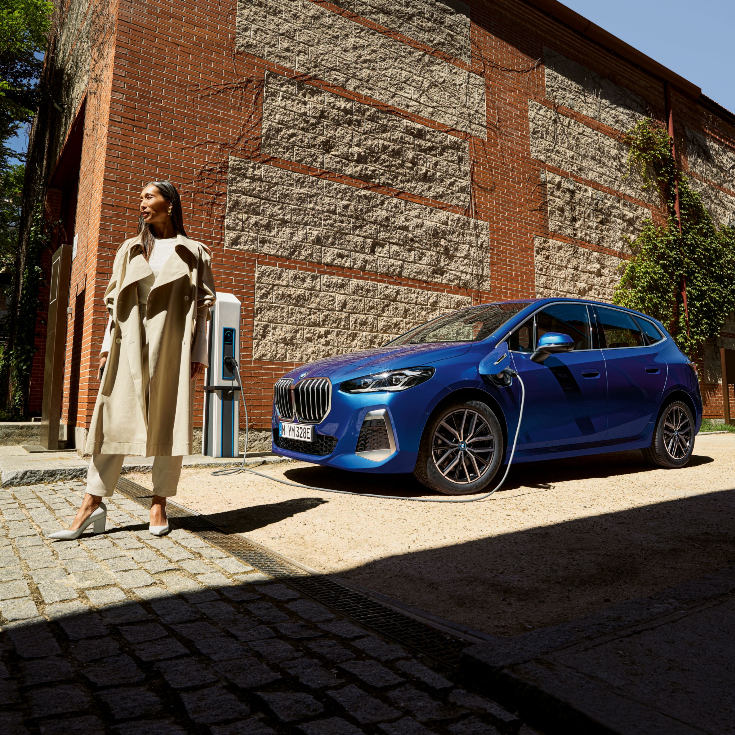 Persoon loopt weg van de BMW 2 Reeks Active Tourer die naast een natuurlijke bakstenen muur via een wallbox aan het opladen is