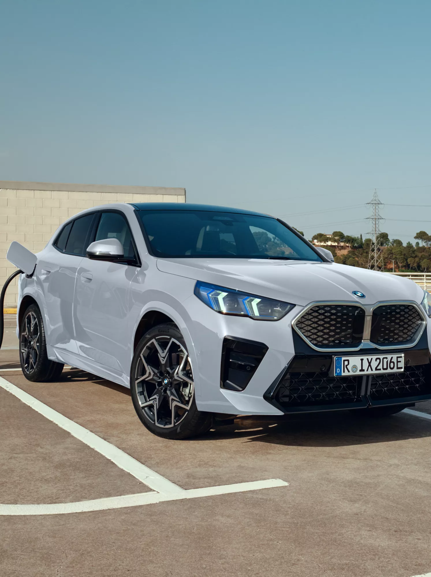 Voiture 100 % électrique BMW iX2 de couleur Brooklyn Grey roulant sur une route au coucher du soleil avec une vue sur l'océan en arrière-plan