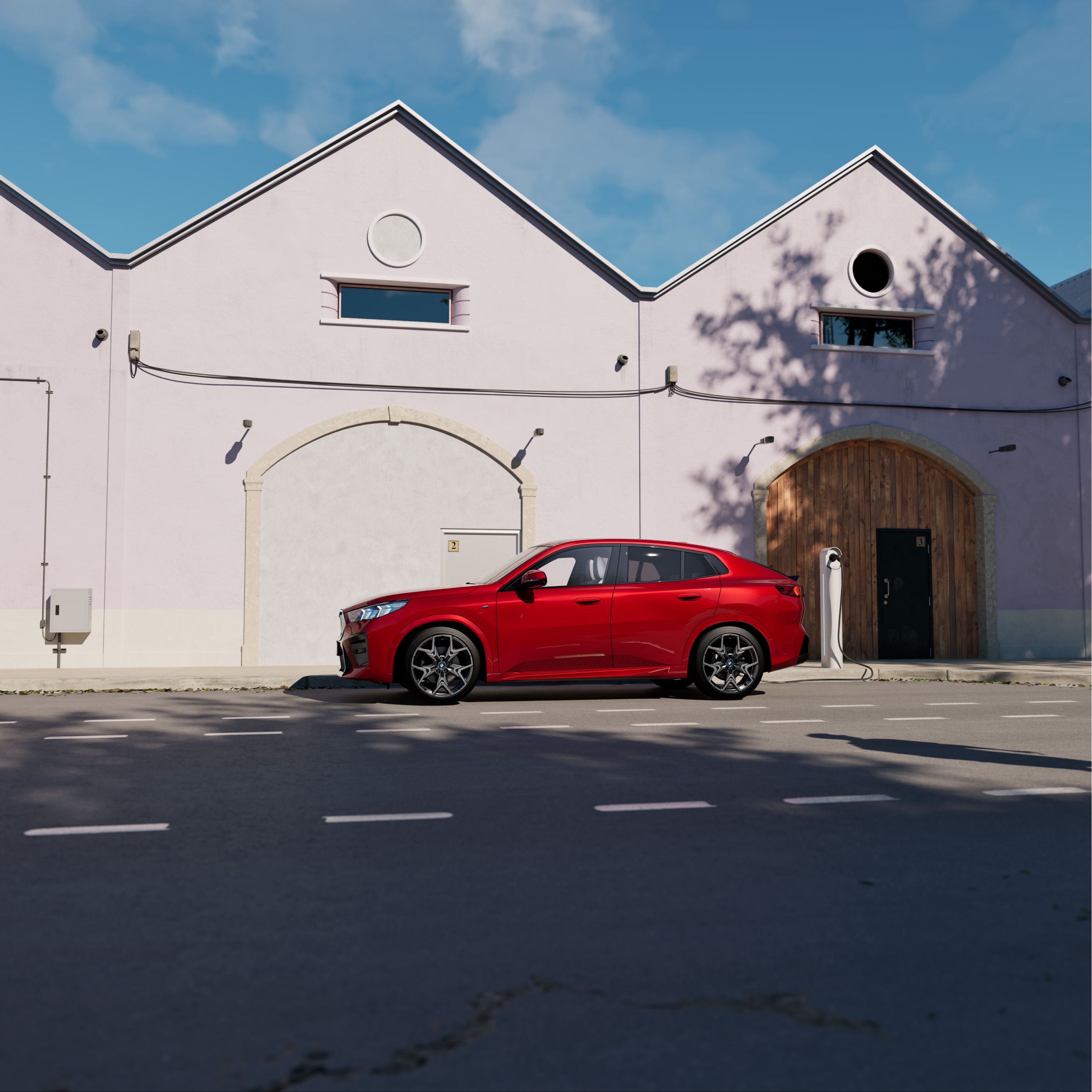 BMW iX2 in Dragonfire Red parcheggiata davanti a una casa di campagna in una giornata di sole