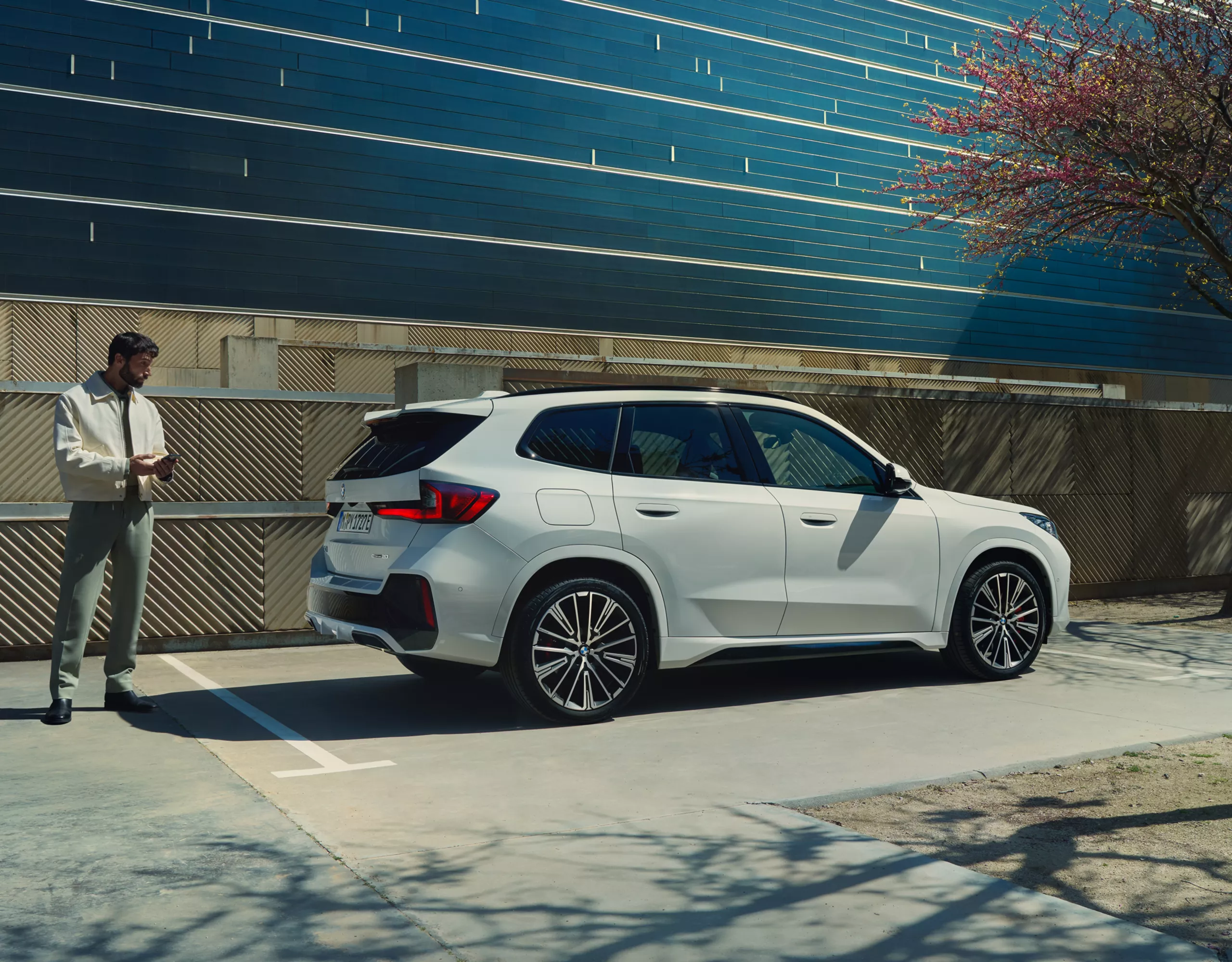 Ein Mann steht auf der Straße vor einem BMW iX1, der lädt.
