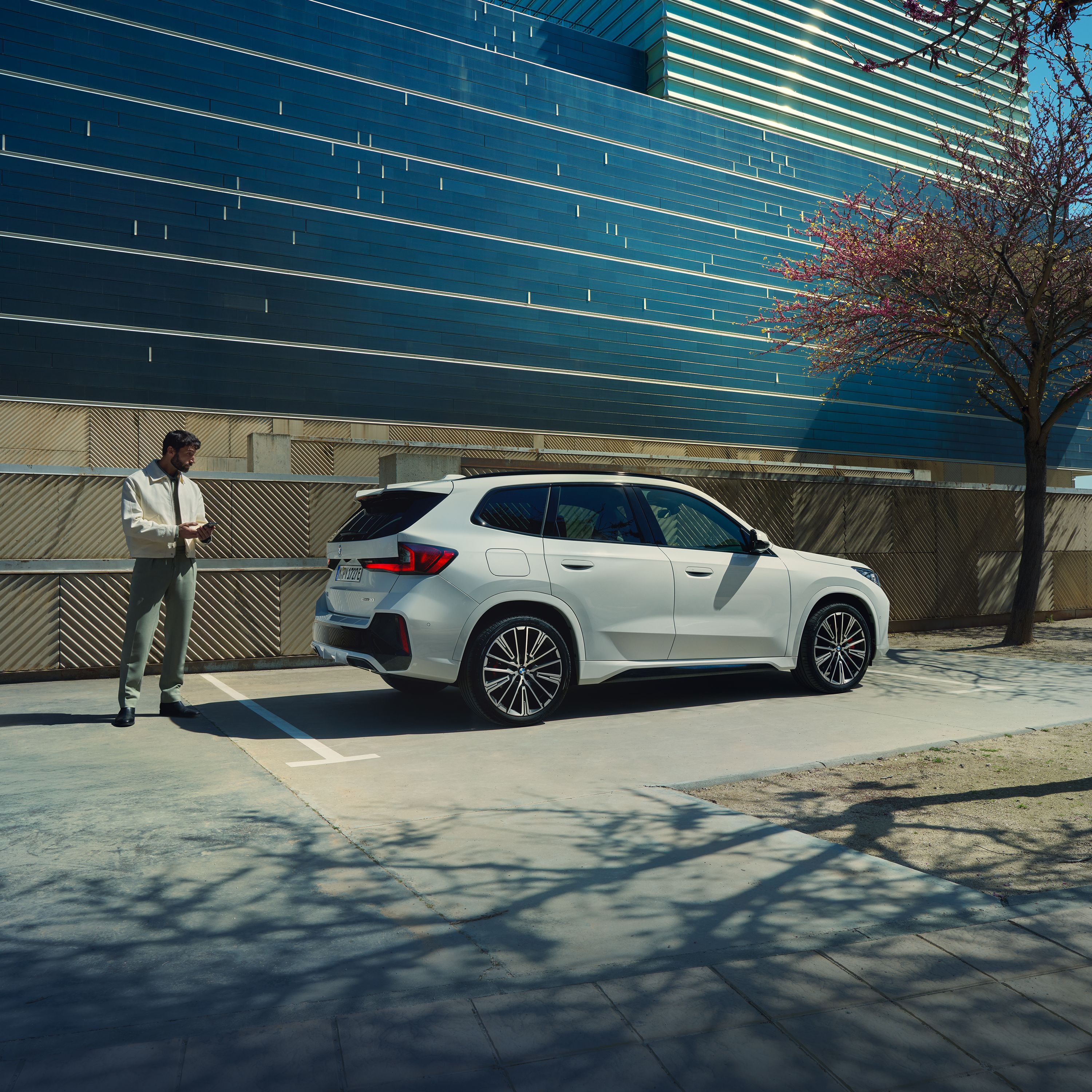 Mężczyzna stoi na ulicy przed ładującym się BMW iX1.