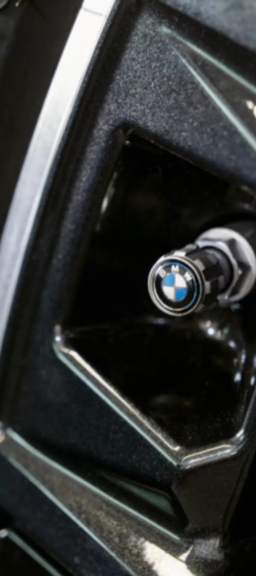 Detalhe de uma jante BMW preta, com foco na tampa da válvula e no pneu.