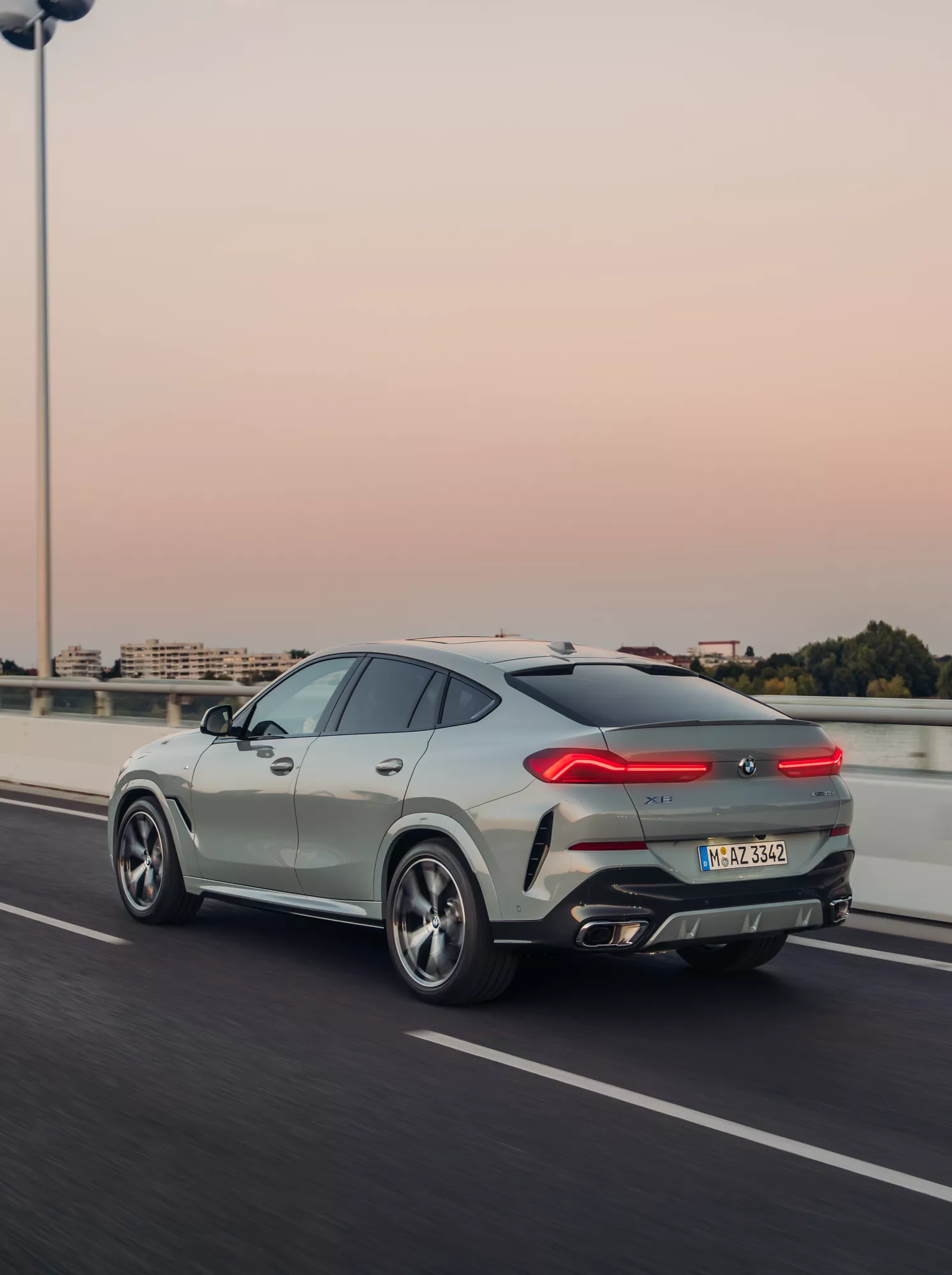 ผู้ชายกำลังเดินเข้าหารถยนต์ BMW X6 ที่จอดอยู่หน้าอาคารทันสมัย