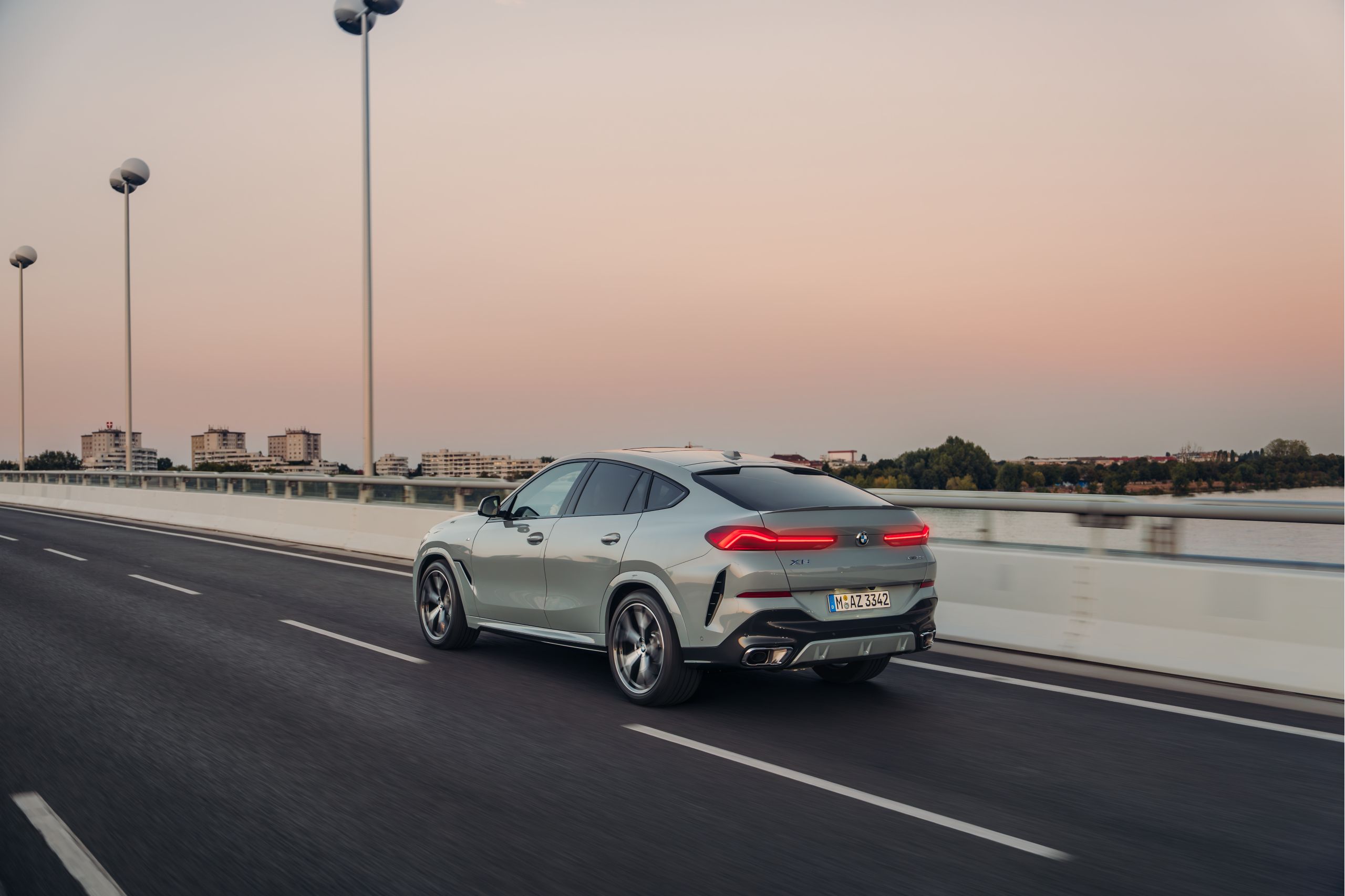 ผู้ชายกำลังเดินเข้าหารถยนต์ BMW X6 ที่จอดอยู่หน้าอาคารทันสมัย