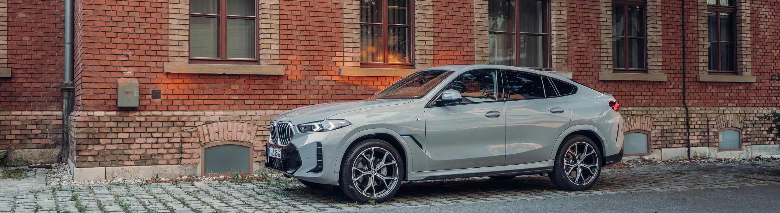 BMW X6 SUV จอดอยู่กลางแสงแดดหน้าตึกอิฐ