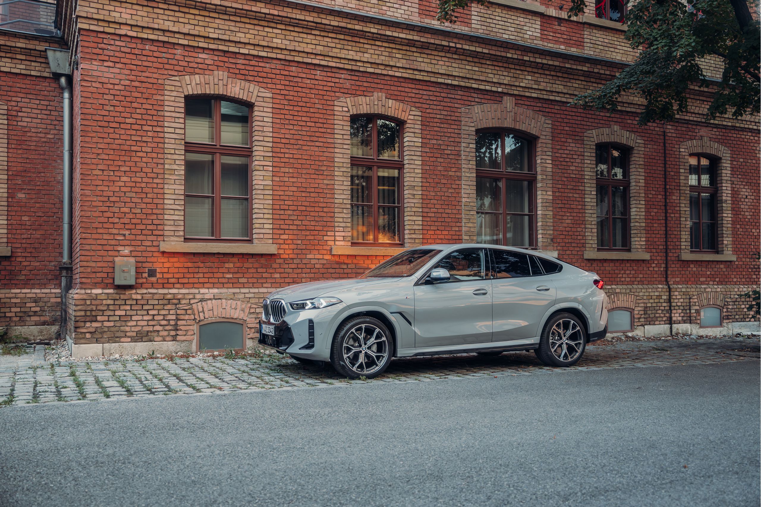 ความโดดเด่นของ BMW X6 SUV ที่จอดอยู่ท่ามกลางแสงแดดด้านหน้าอาคารอิฐ