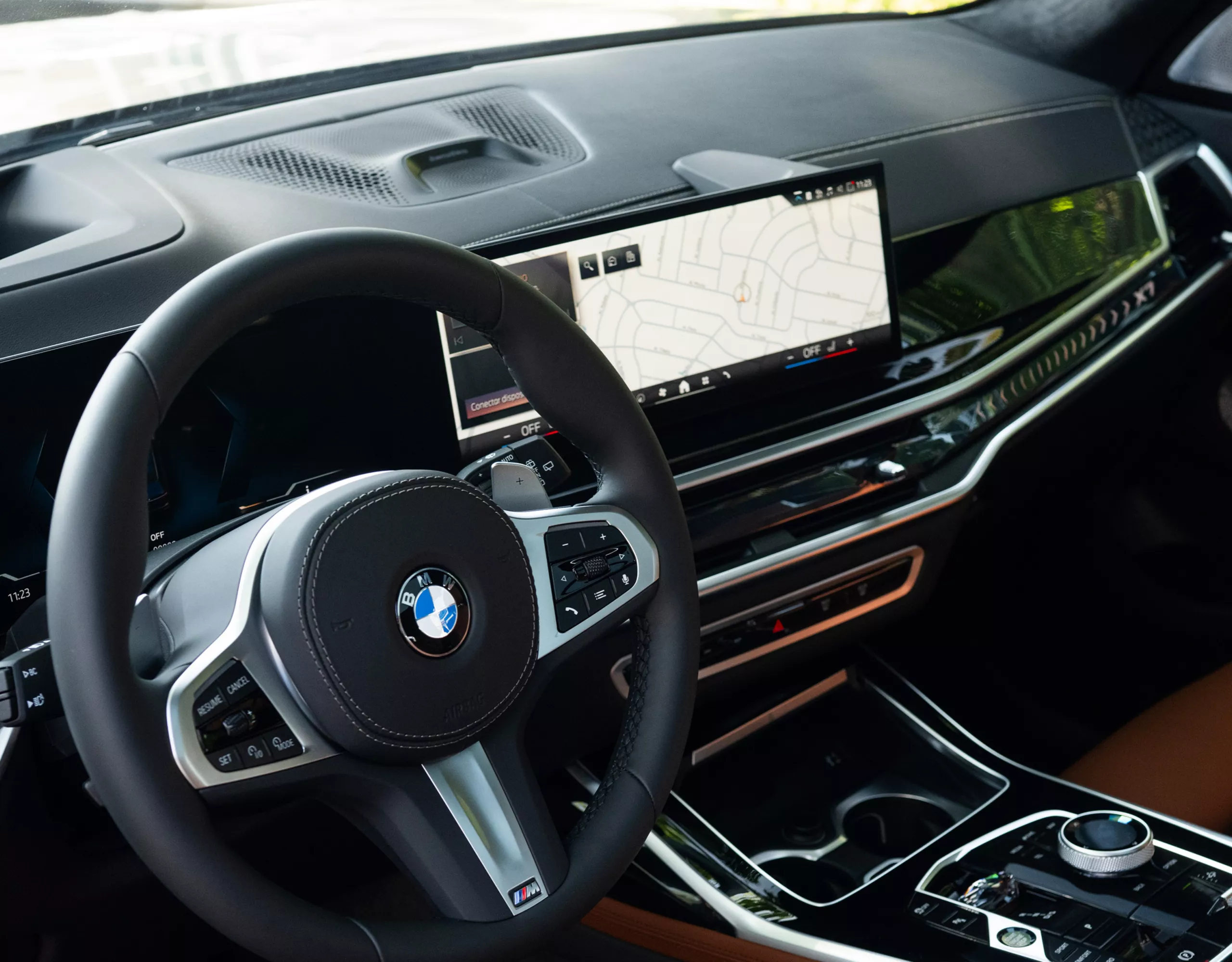 Interior do BMW X7 com assentos em couro, cockpit, decoração em madeira, teto panorâmico de vidro, console central e fileiras traseiras de assentos