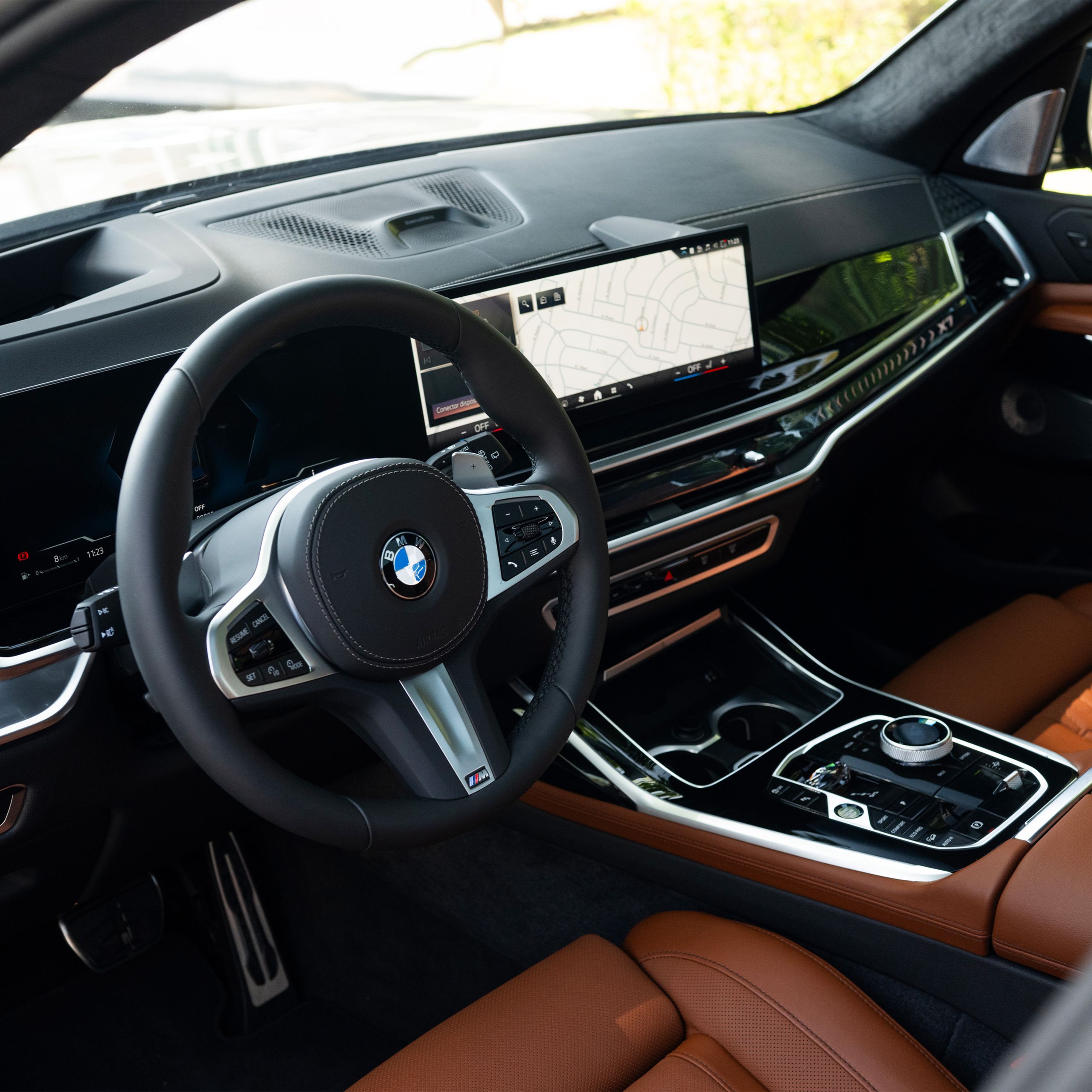 Interior do BMW X7 com assentos em couro, cockpit, decoração em madeira, teto panorâmico de vidro, console central e fileiras traseiras de assentos